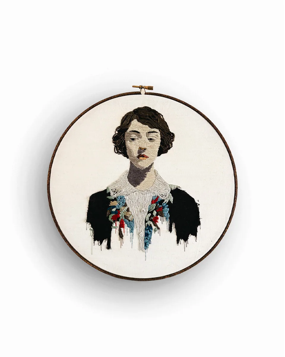 Embroidered cloaked figure displayed in a round hoop