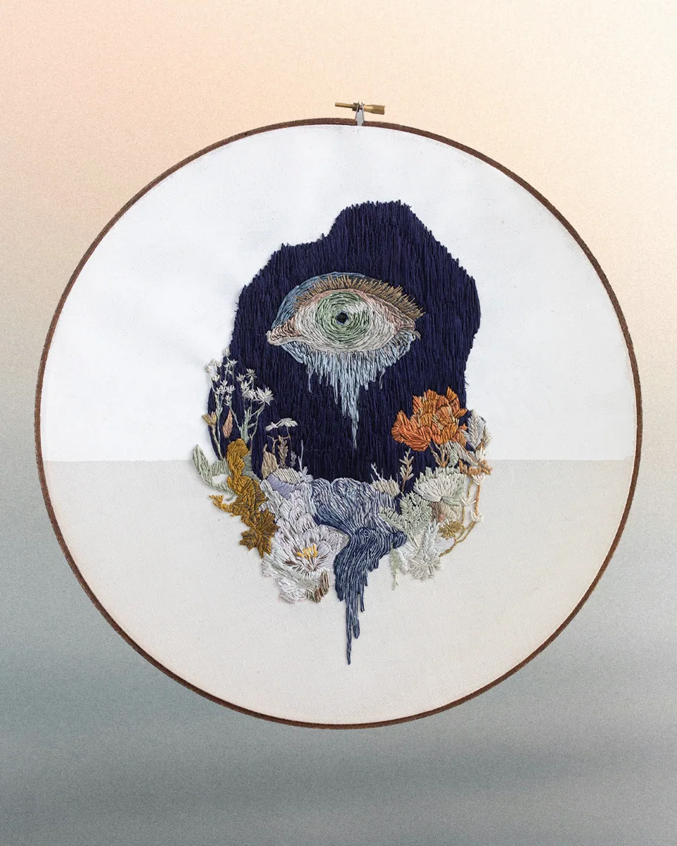 Round embroidery featuring an eye, raven, and flowers