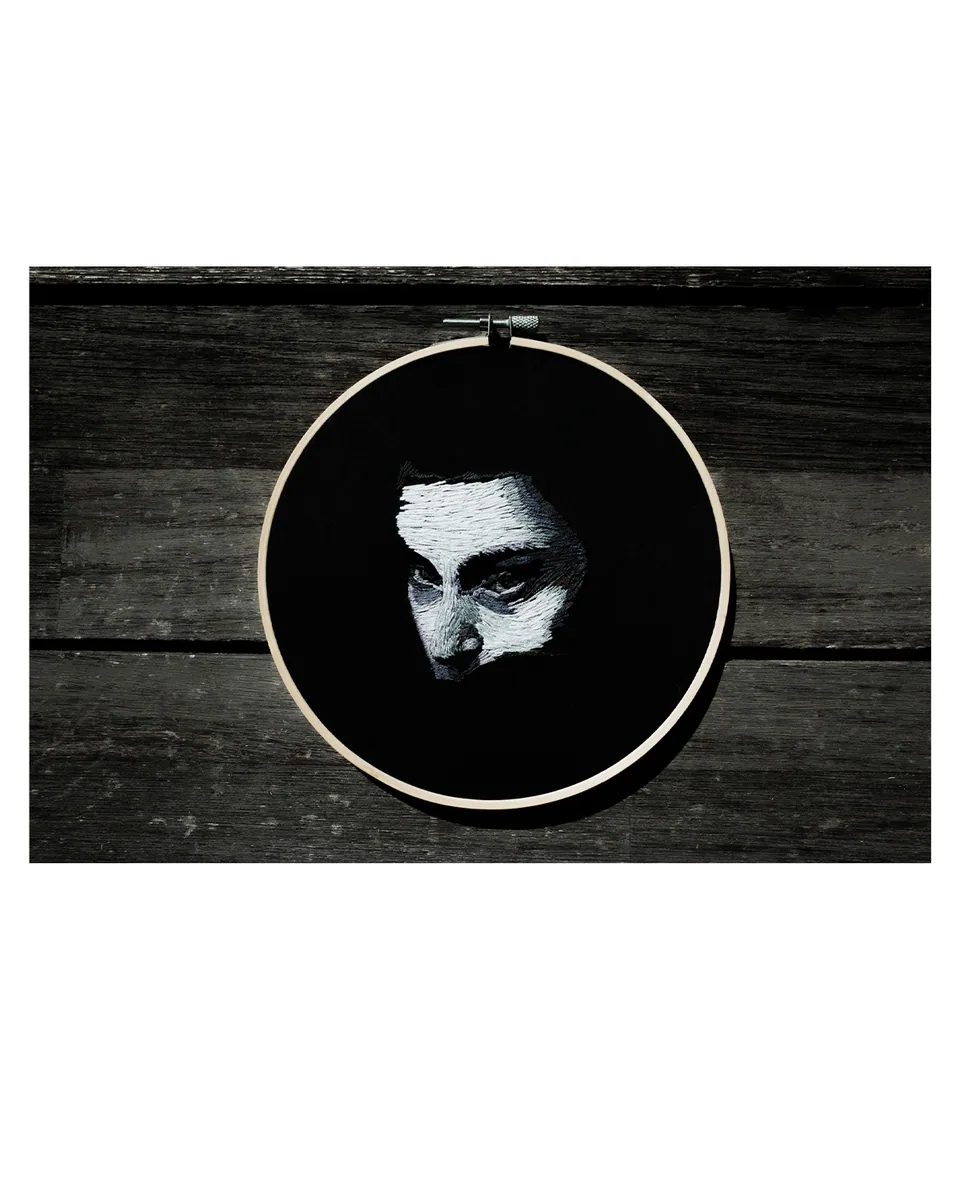 Monochrome embroidered face displayed in a round hoop
