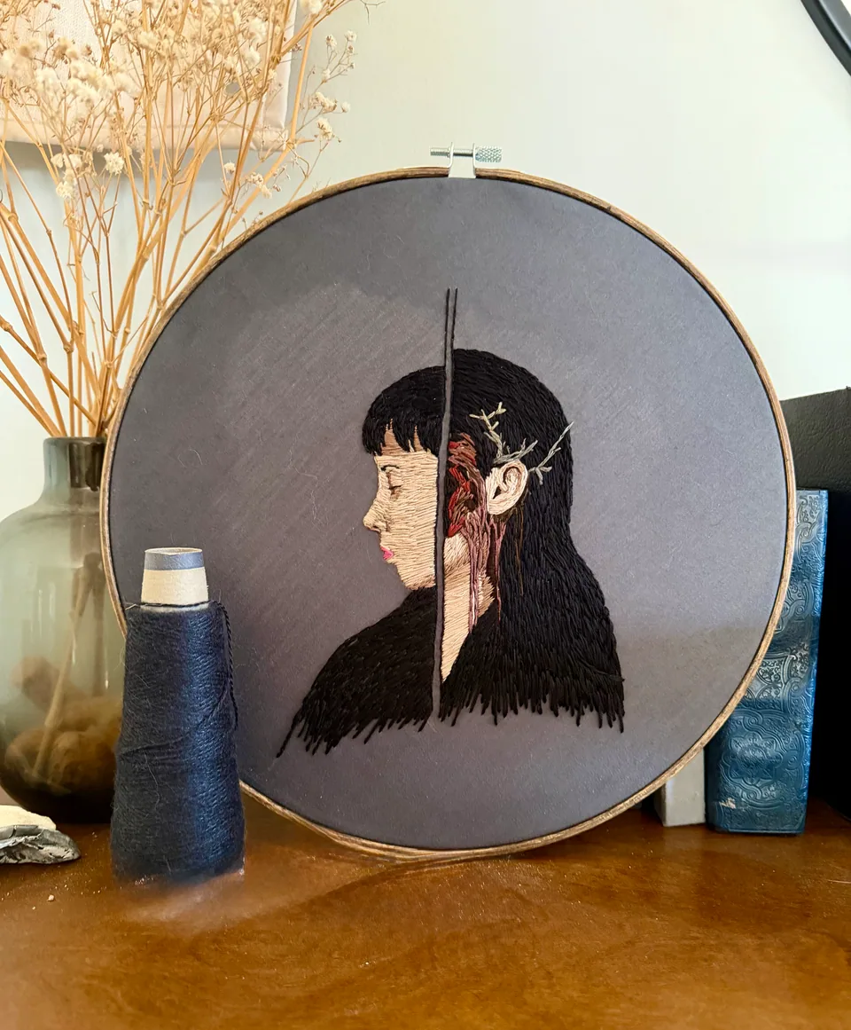 Embroidered side-profile portrait divided by a dark vertical line