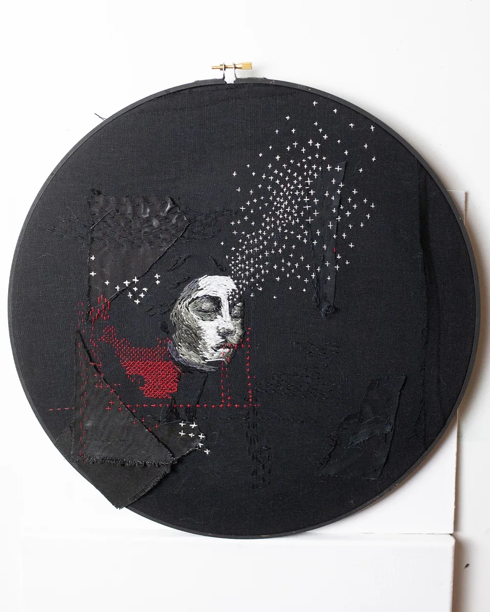 Dark round embroidery with a solitary figure and stitched stars