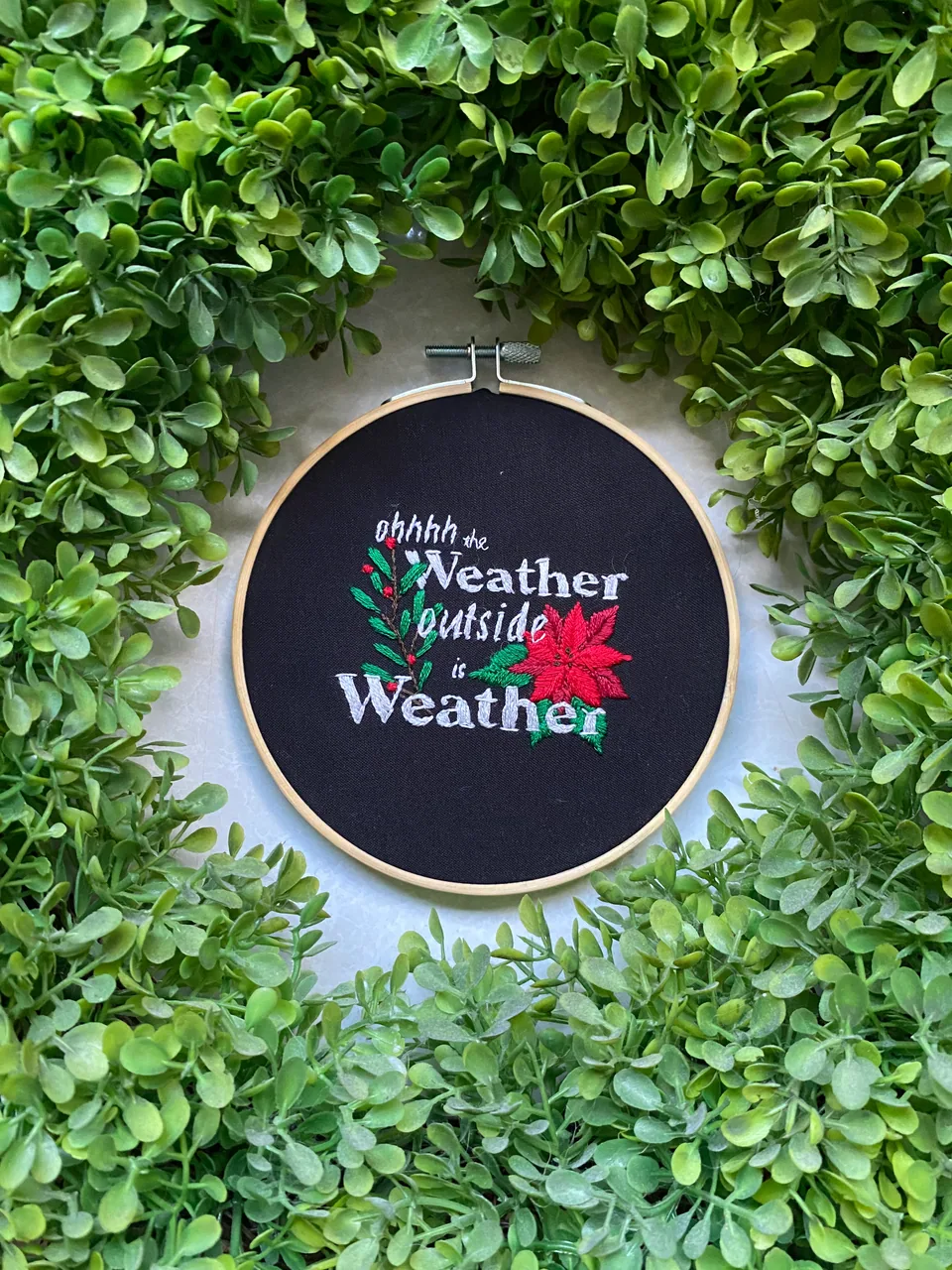 Festive hand-lettered hoop embroidery framed by greenery